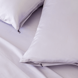 Close-up of light lavender pillows with concealed zipper closures and small black branded zipper pulls.