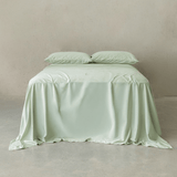 Sage green bamboo cotton sheet set styled on a bed with matching pillowcases, showcasing a smooth finish, elegant drape, and calming minimalist aesthetic.