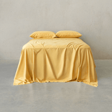 Warm golden yellow bed sheet set draped over a double bed with two matching pillowcases against a neutral wall