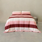 Pink, blush, cream, and burgundy striped quilt cover set with matching pillowcases displayed on a neatly made bed in a modern minimalist bedroom.