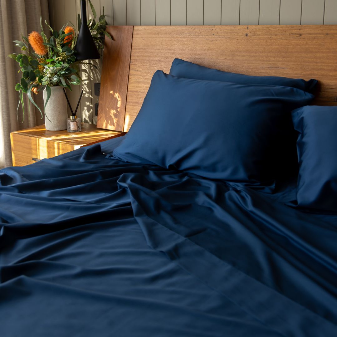 Navy blue bedding set on a bed with a wooden headboard and decorative plants.