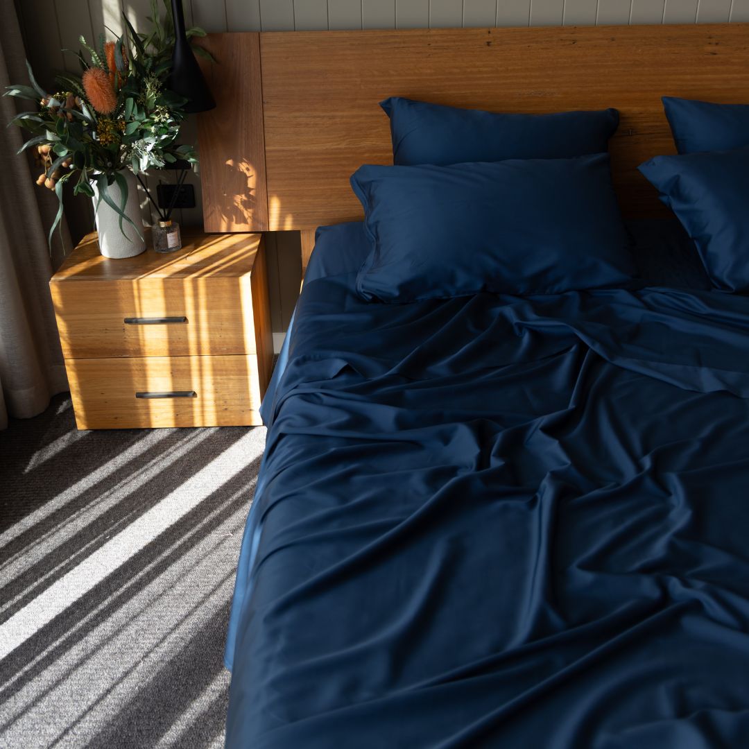 Bedroom with wooden headboard and nightstand, featuring blue bedding and a plant.