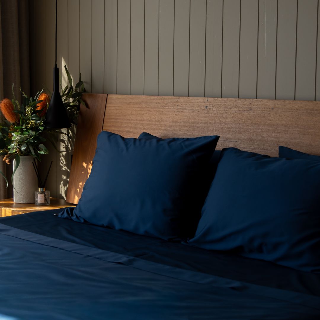 Bed with blue pillows and a wooden headboard in a room with plants and decor.
