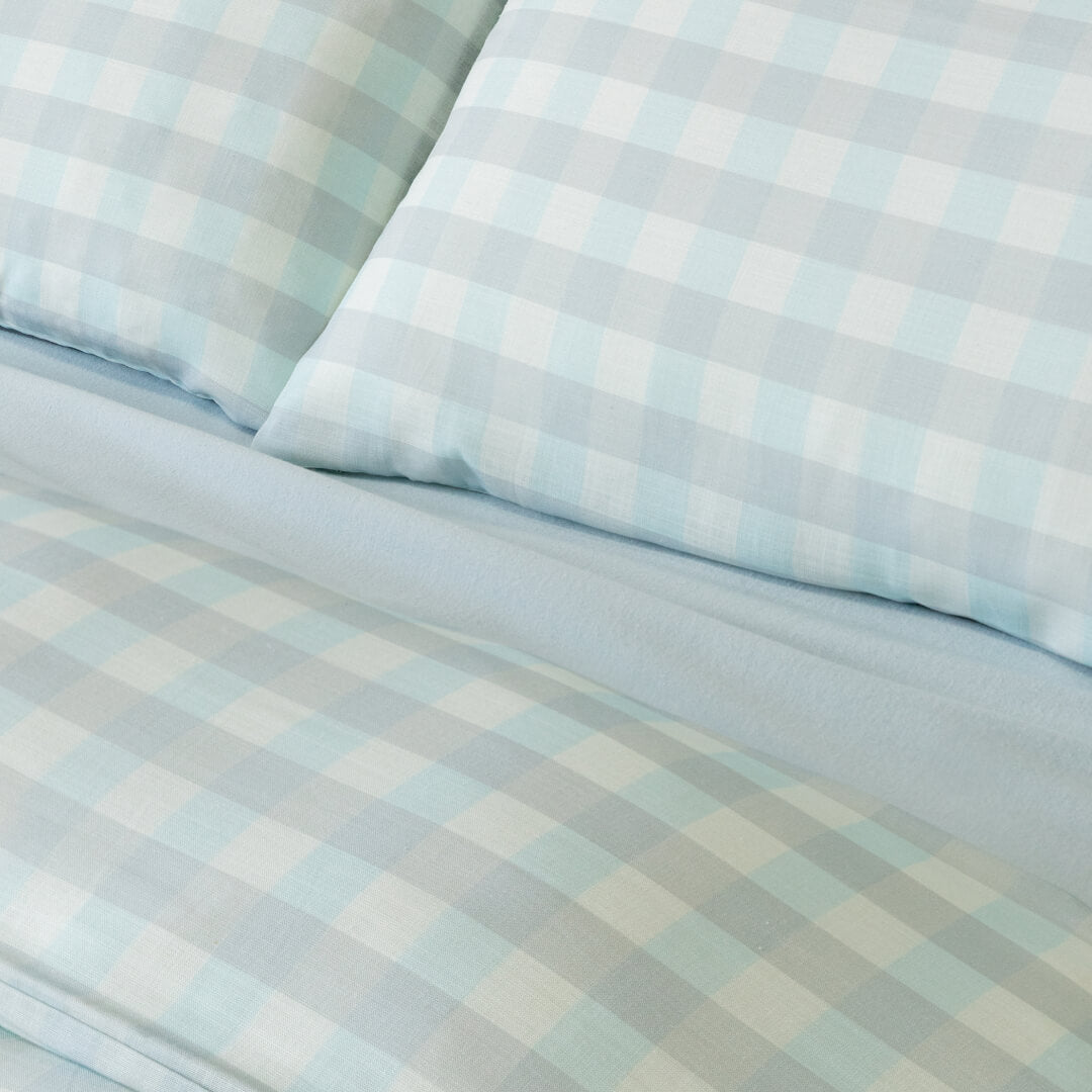 Close-up of light blue gingham bedding with matching pillowcases and a soft blue fitted sheet, highlighting the subtle check pattern and coordinated color palette