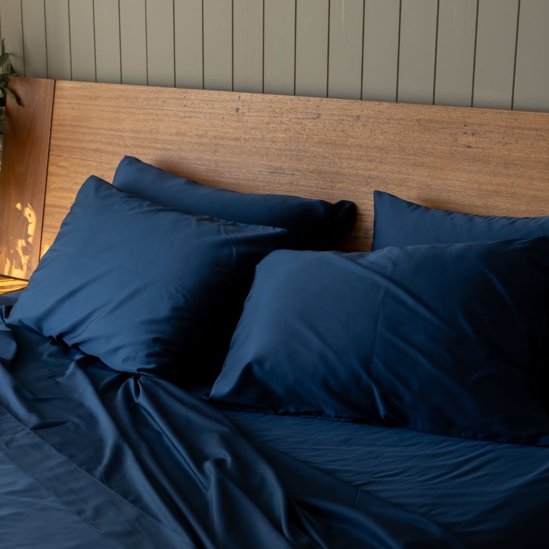 Bed with blue bedding and pillows against a wooden headboard.