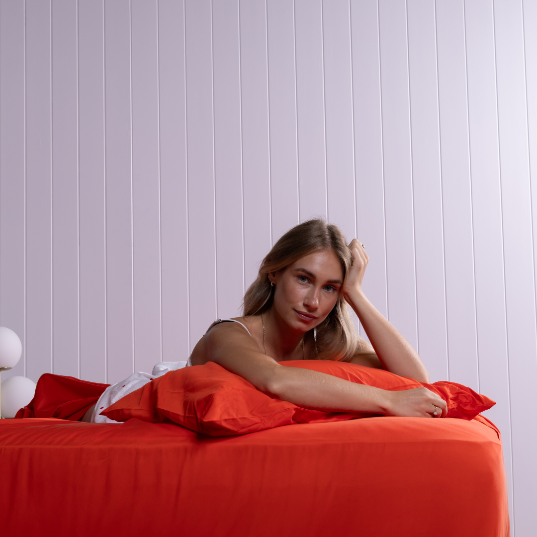 Relaxed woman lounging on red bamboo cotton bed sheets, emphasising breathable and soft fabric.