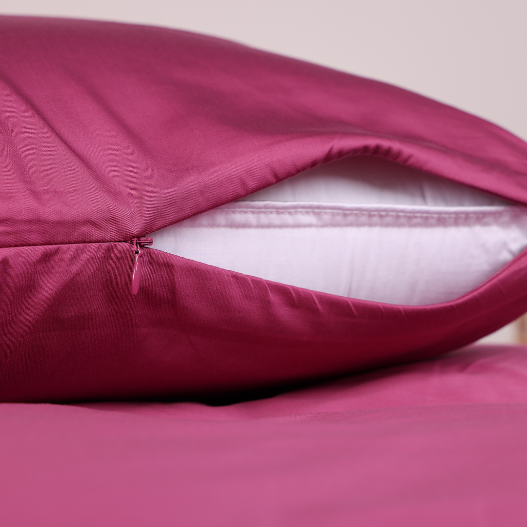 A pink bed with matching pillows and wooden bedside tables with small plants.