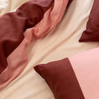Pink, cream, and burgundy striped quilt cover and pillowcases layered over soft neutral sheets, highlighting the fabric drape, texture, and warm color palette.