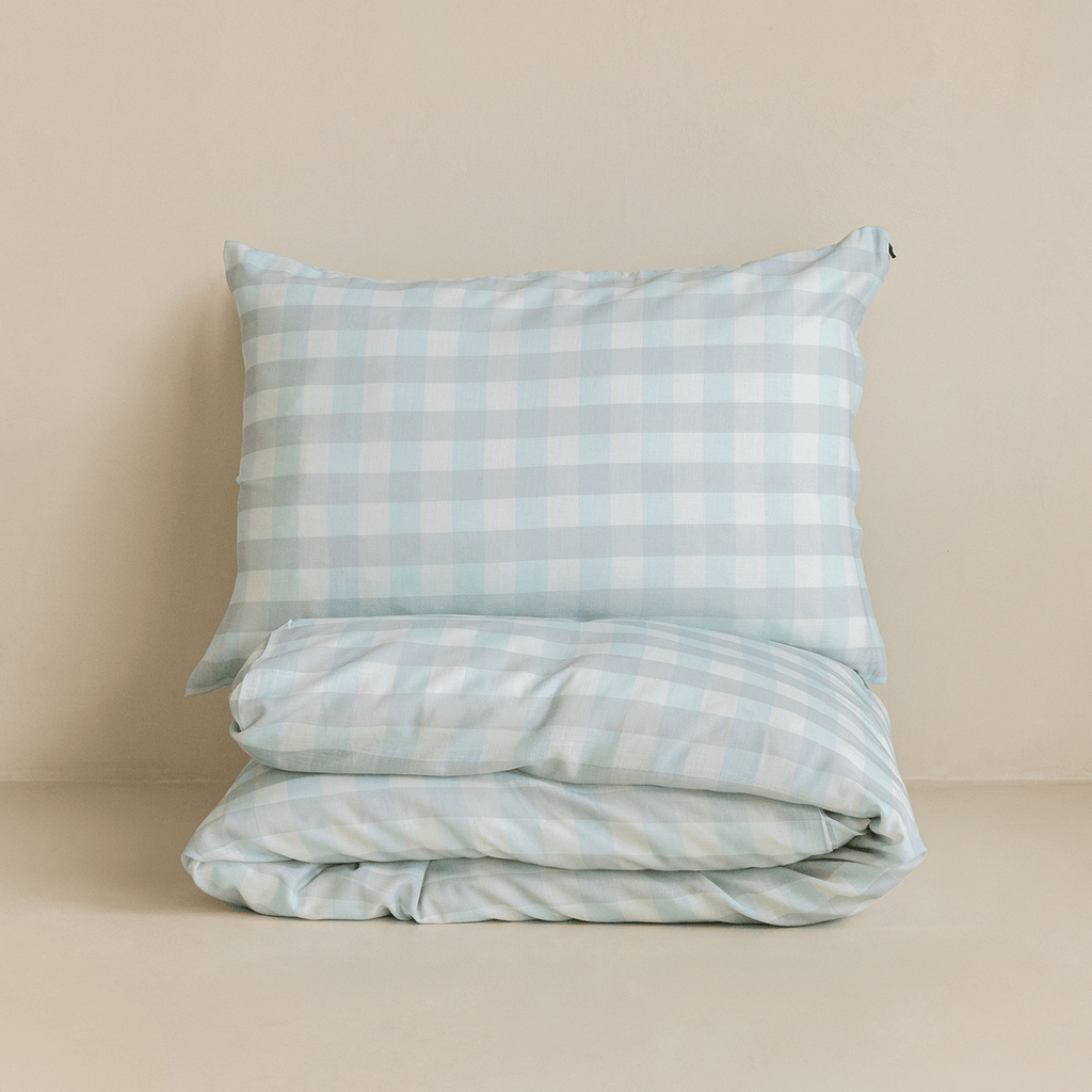 Folded light blue gingham quilt cover set with a matching pillowcase stacked neatly, highlighting the classic check pattern and soft, breathable fabric.