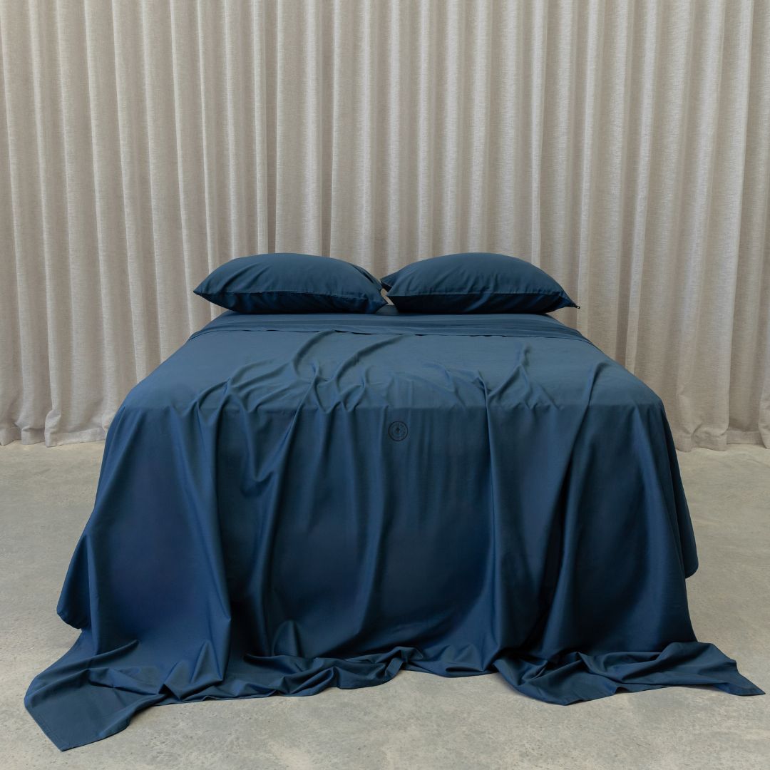 Blue bedspread on a bed with pillows against a beige curtain background