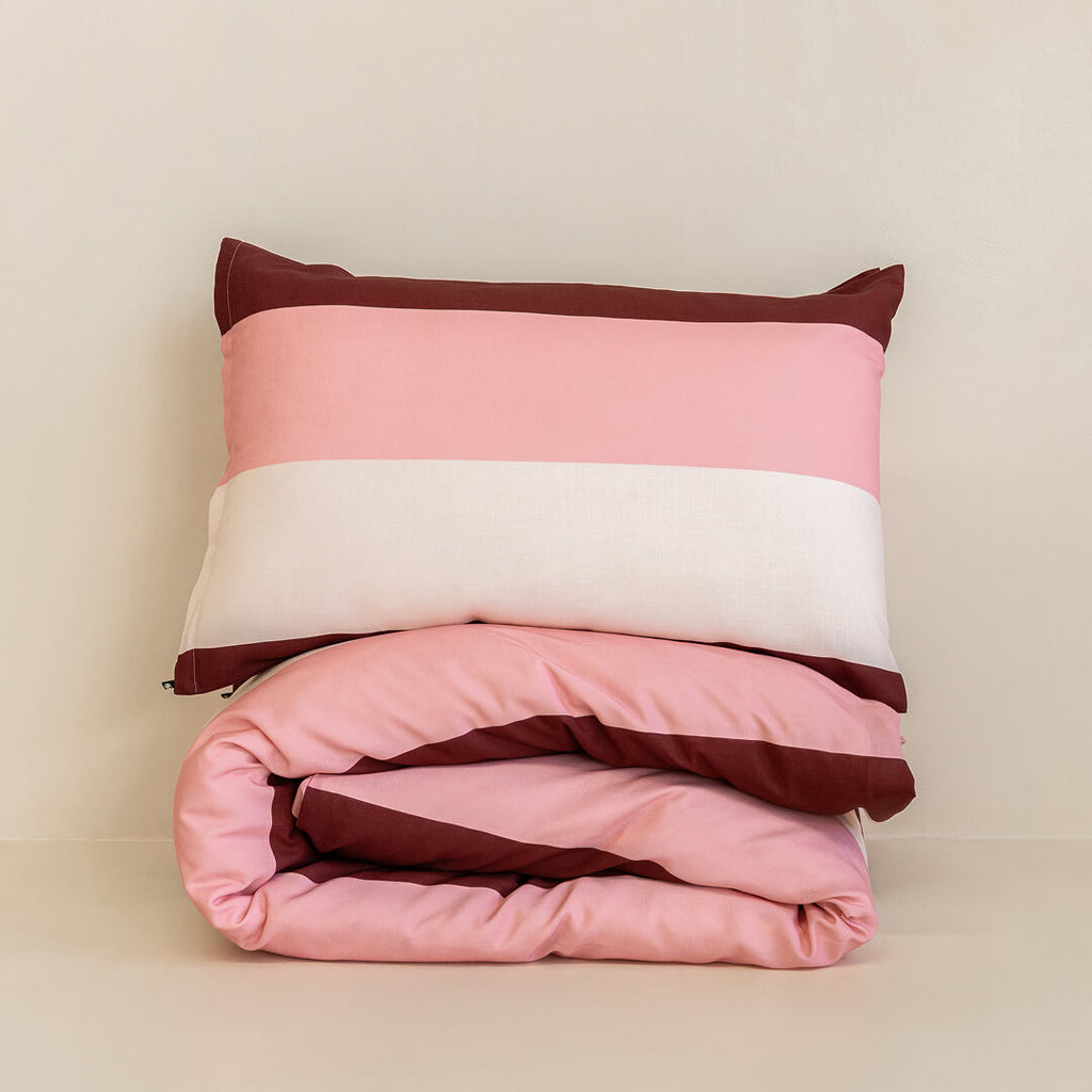 Folded striped quilt cover set with a matching pillowcase in blush pink, cream, and burgundy tones, neatly stacked to showcase the bold stripe pattern and soft fabric.