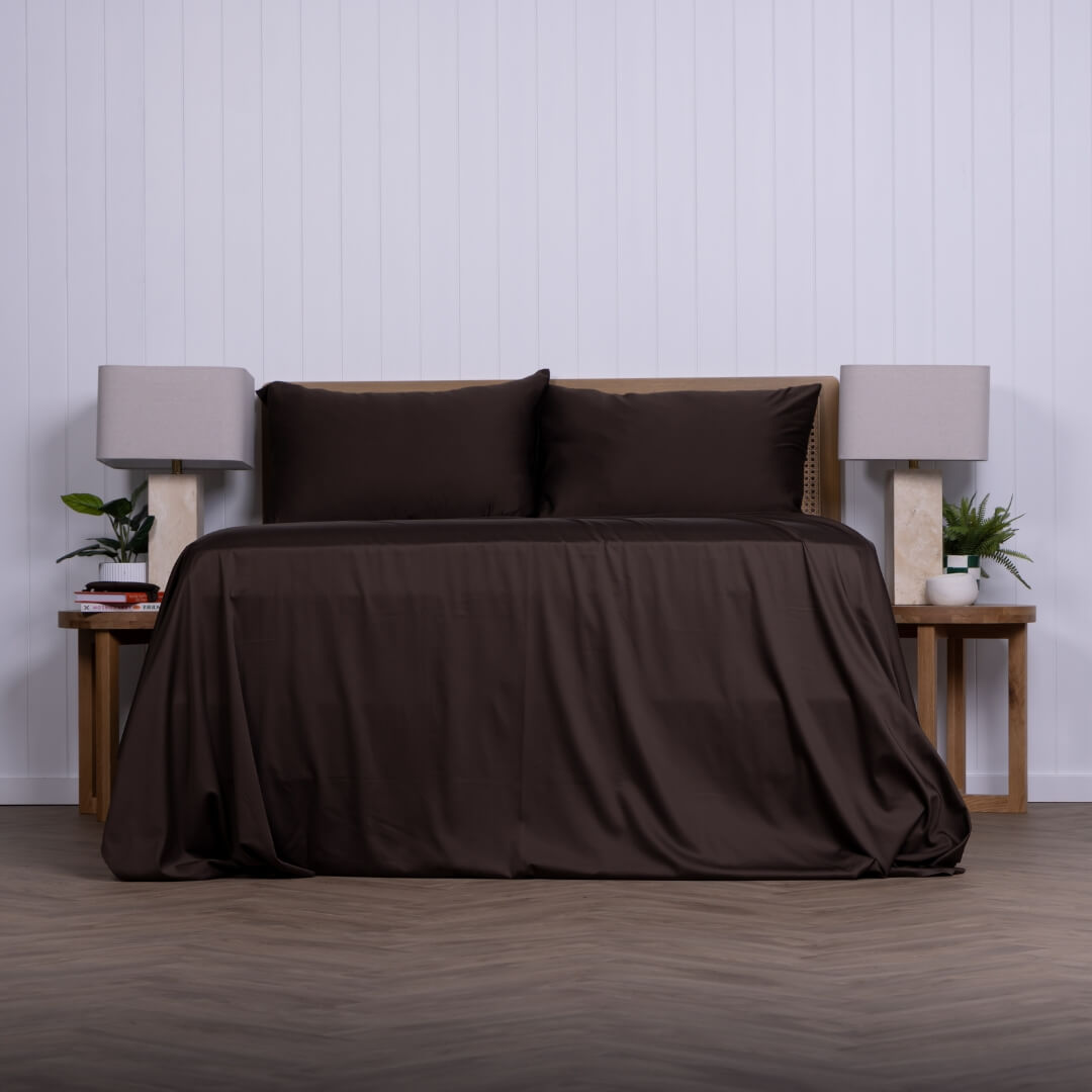 Brown sheet set on a bed with matching pillows in a minimalistic bedroom setting.
