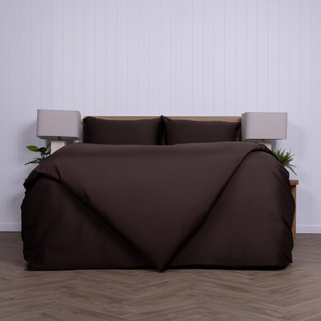Brown bedspread on a bed with a white wall and wooden floor in the background.