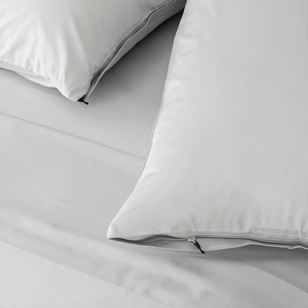 Close-up of light gray pillowcases with concealed zipper closures and small black zipper pulls on matching bedding.