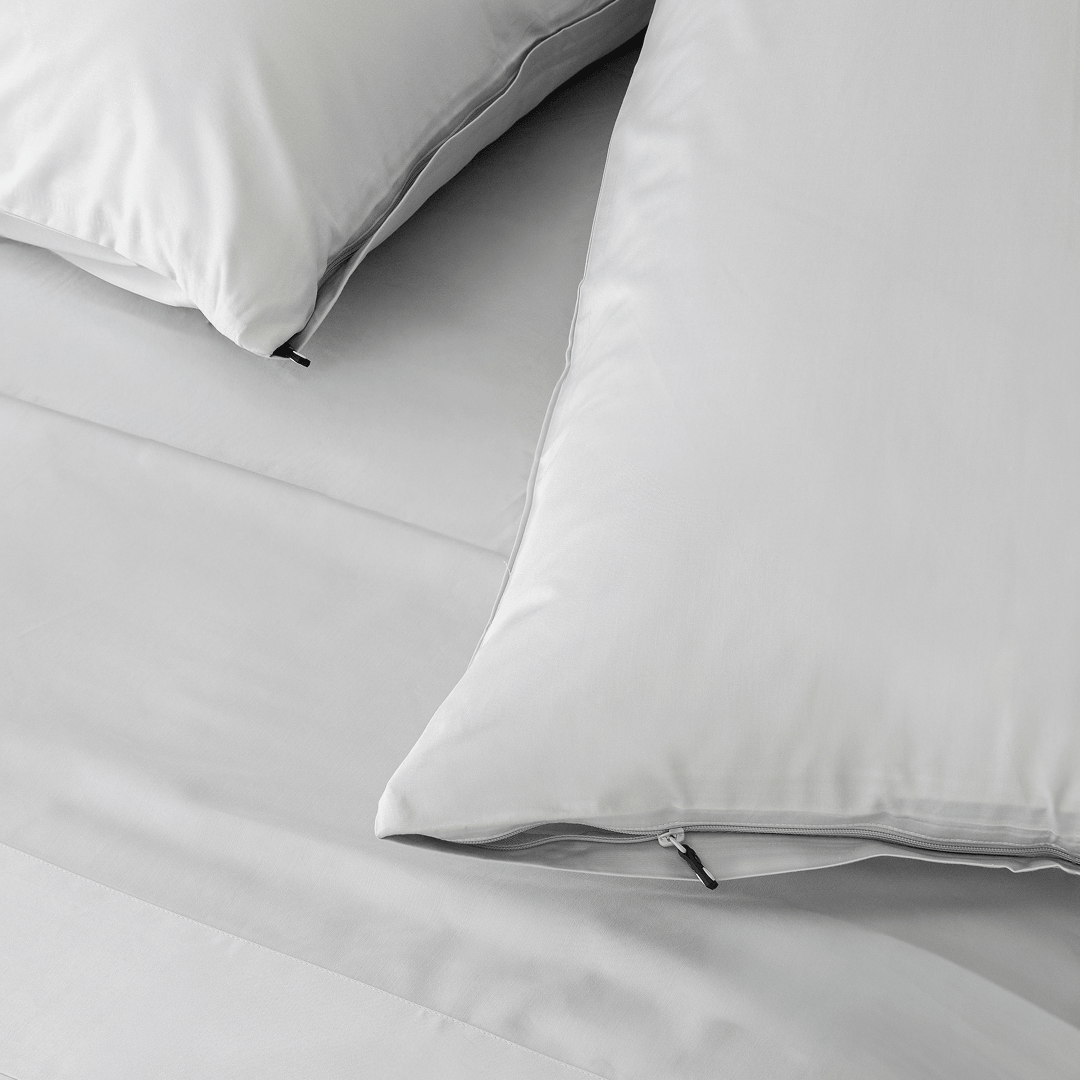 Close-up of light gray pillowcases with concealed zipper closures and small black zipper pulls on matching bedding.