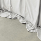 Close-up of a light gray flat sheet draping softly onto a concrete floor, showing its smooth texture and flowing folds.