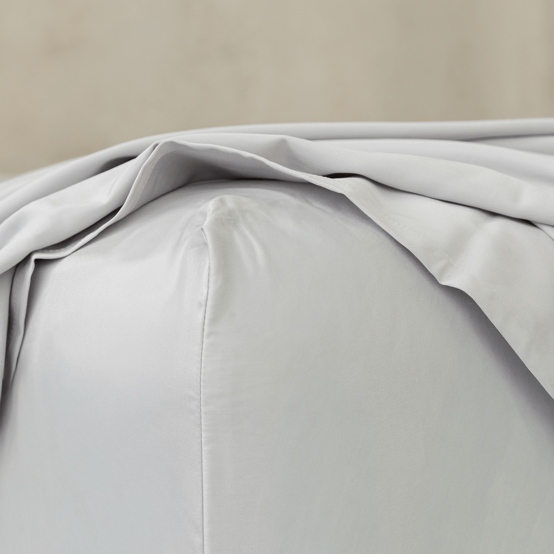 Close-up of a light gray flat sheet draping softly onto a concrete floor, showing its smooth texture and flowing folds.