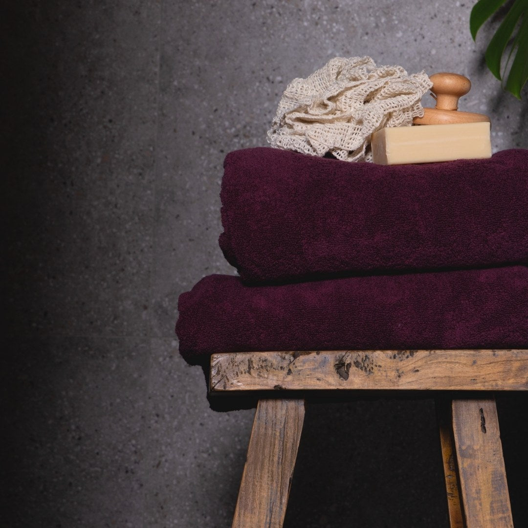 Two burgundy towels on a wooden stand with a textured grey background.
