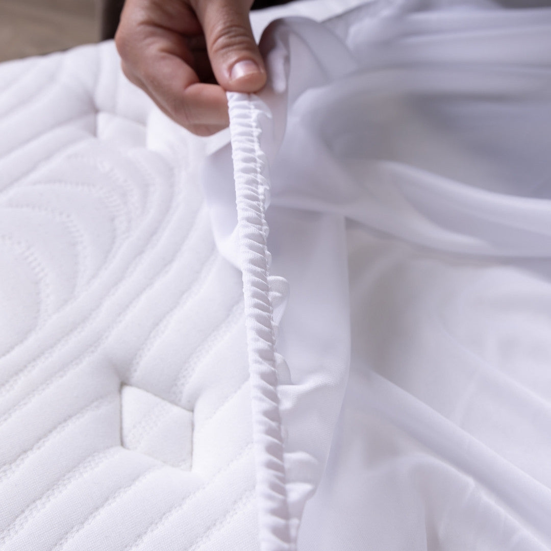 Close-up of a hand holding white quilted fabric, elastic edge of the mattress protector.
