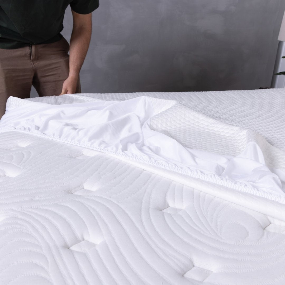 Person standing next to a white mattress with a mattress protector being put on top.