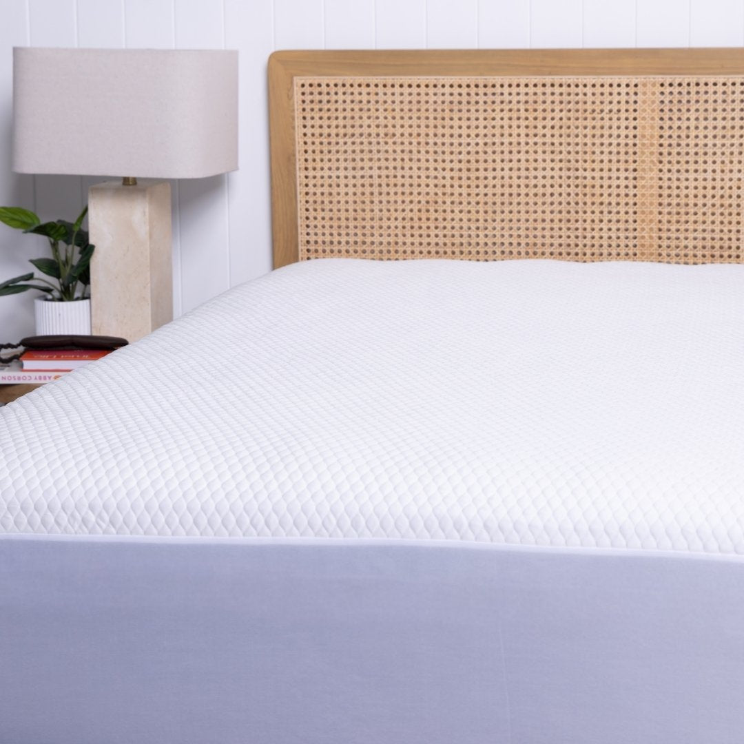 Bed with white mattress protector and wooden headboard in a bedroom setting.