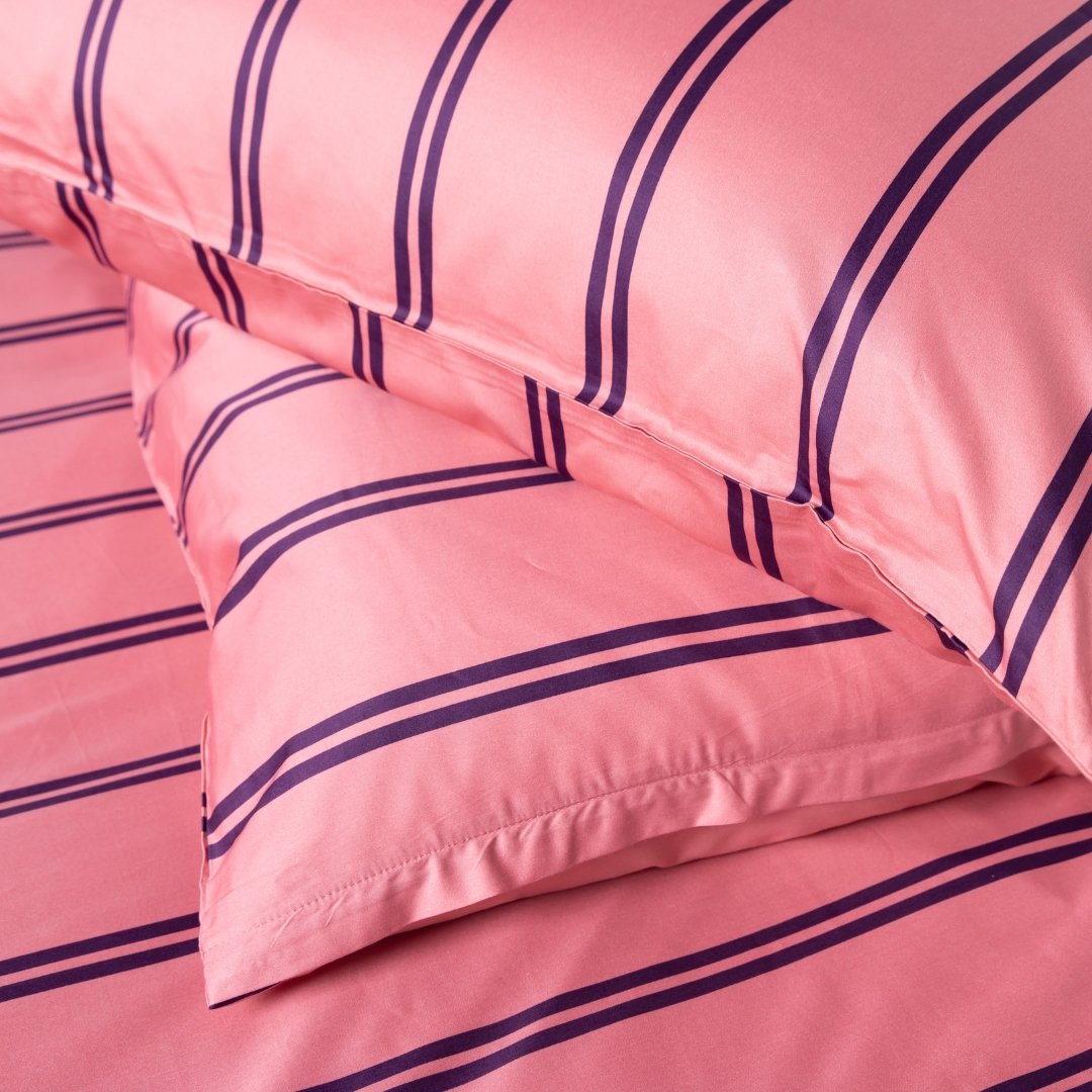 Pink bed sheets with purple stripes on a soft focus background.