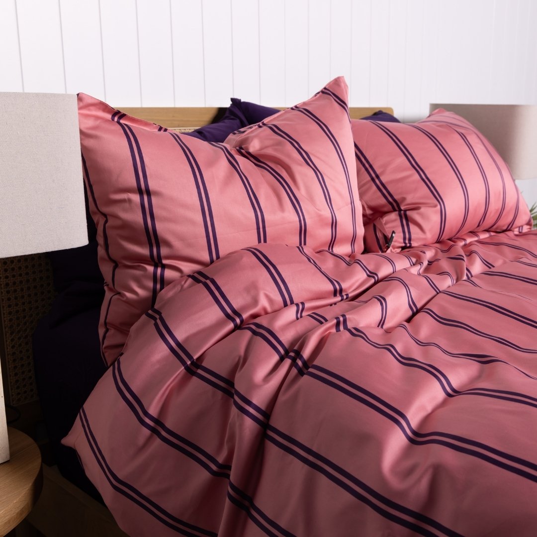 Pink and purple striped bedding set on a bed with a timber headboard.