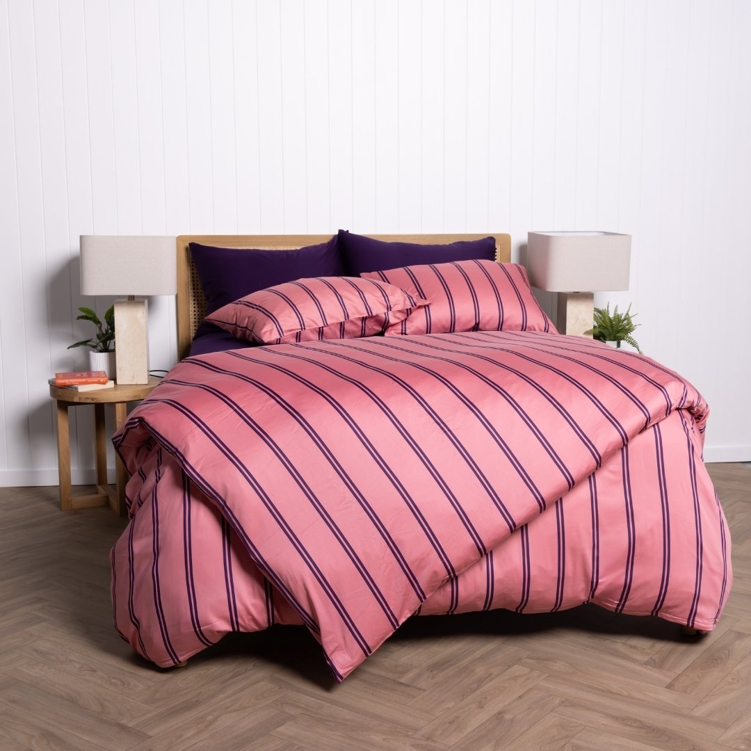 Bed with pink and purple striped bedding in a room with lamps and a plant.