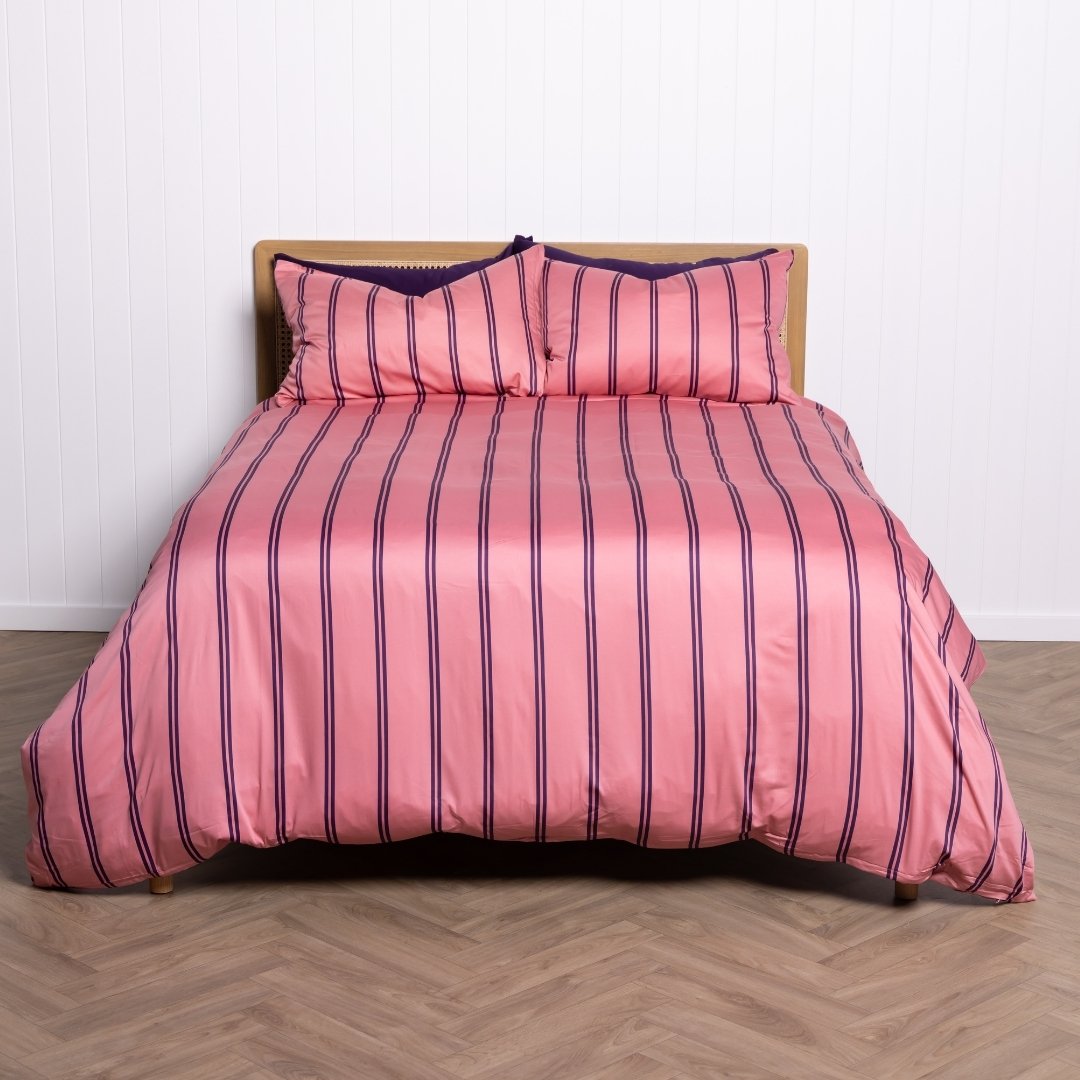 Pink striped bedspread with matching pillows on a wooden bed frame against a white wall.
