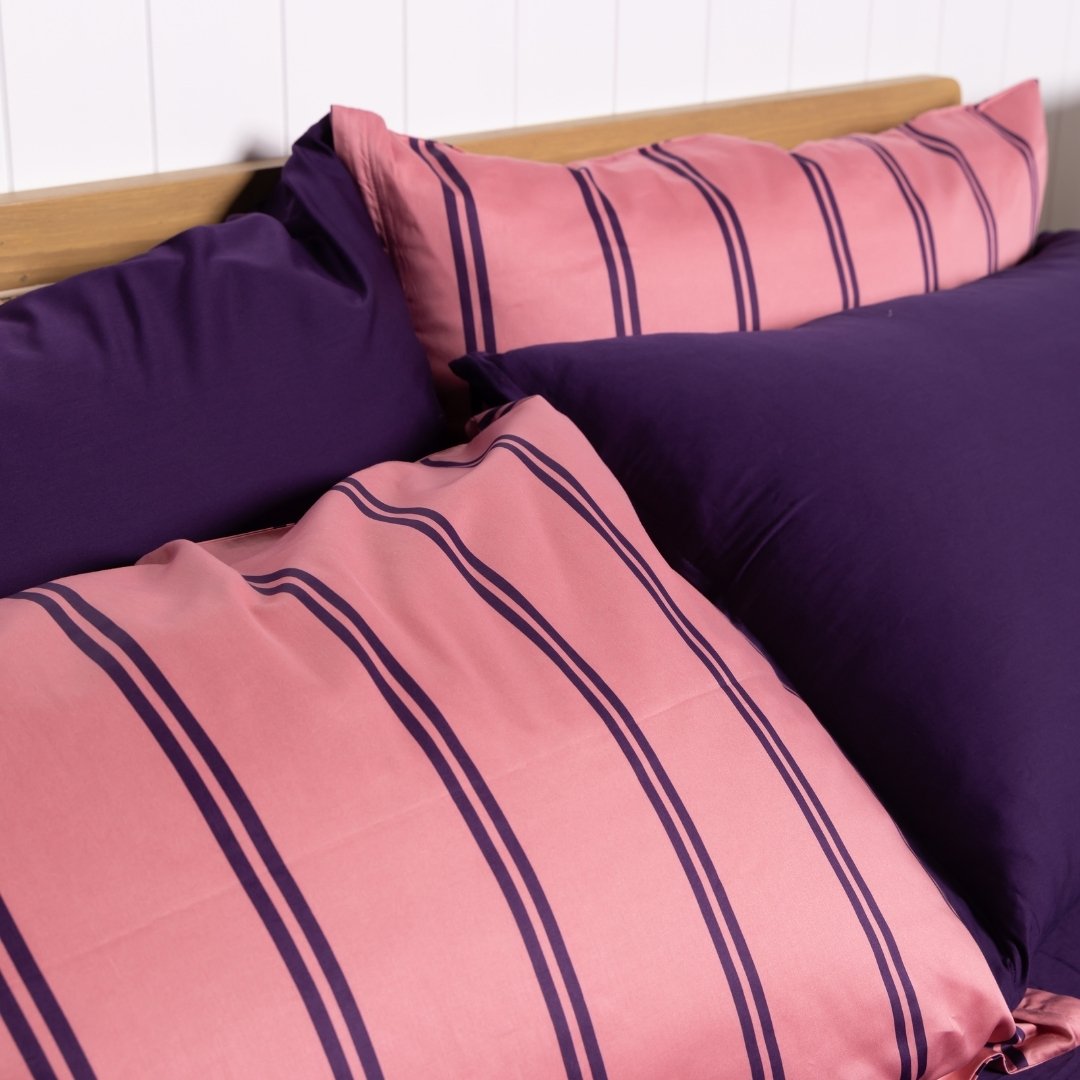 Pink and purple striped pillows on a bed with a white wall background.