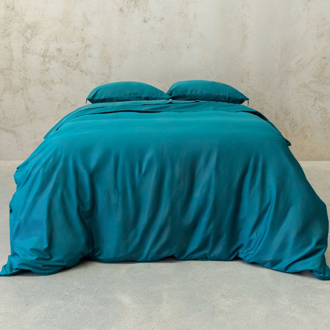 Teal bedspread and pillows on a bed against a beige wall.