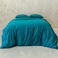 Teal bedspread and pillows on a bed against a beige wall.