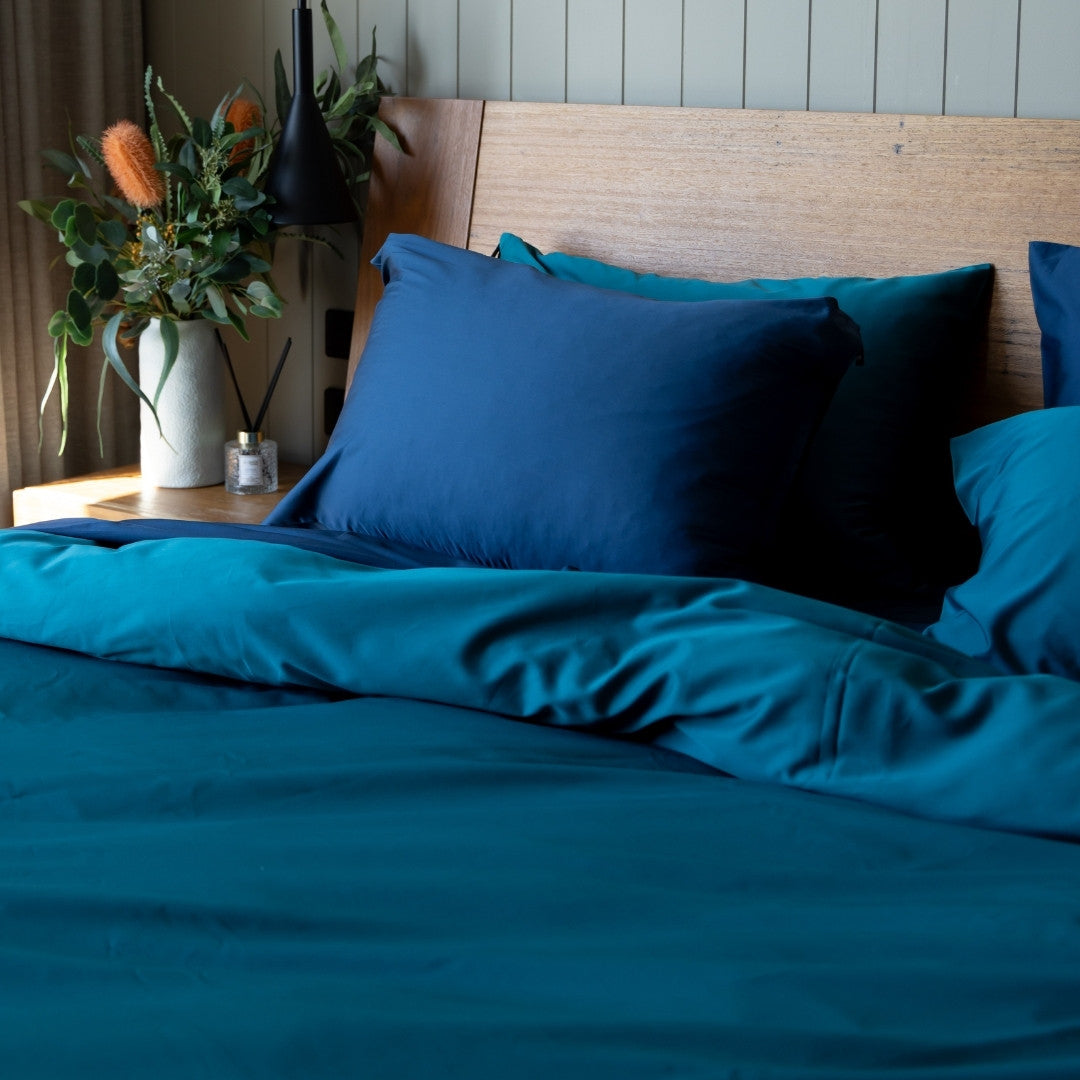 Teal & Navy bedding set on a bed with a wooden headboard and decorative plants.