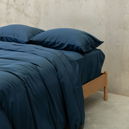 Bed with dark blue bedding and wooden headboard against a neutral wall.