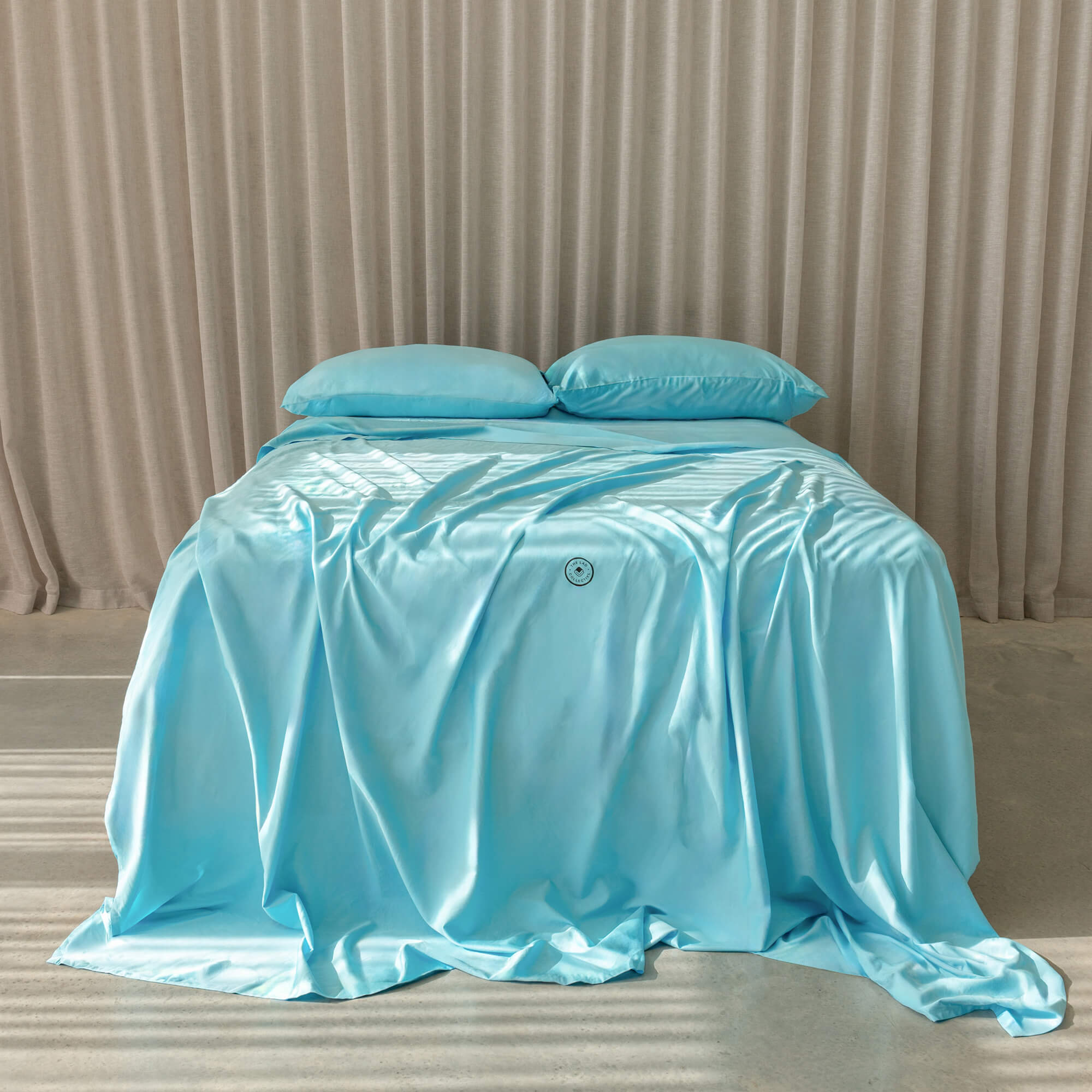 Light blue satin sheet set on a bed with a neutral background