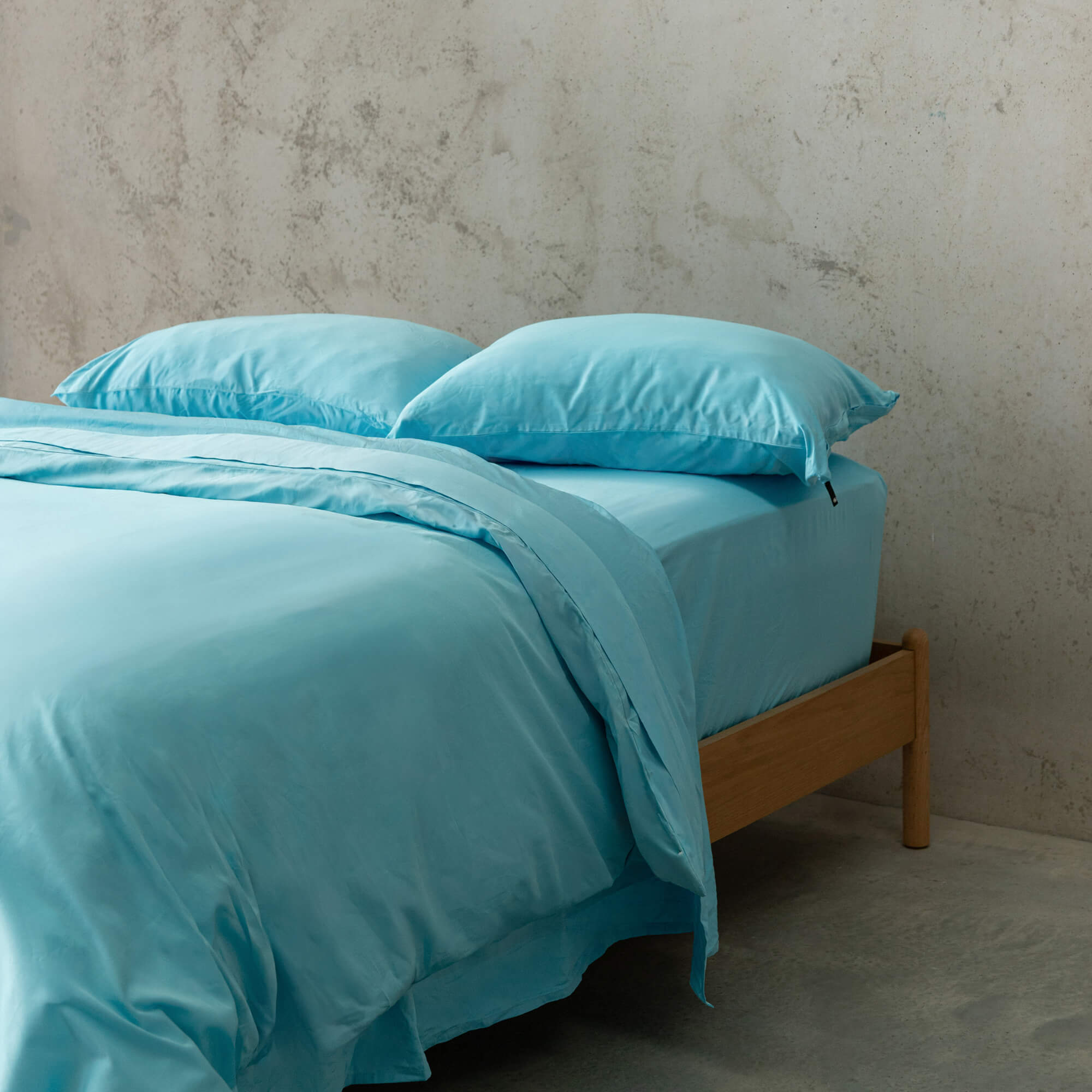 Light blue quilt cover set on a wooden bed against a concrete wall.