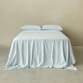 Light blue fitted sheet set styled on a neatly made bed with matching pillowcases, showcasing a clean, minimalist bedroom aesthetic and soft fabric drape.