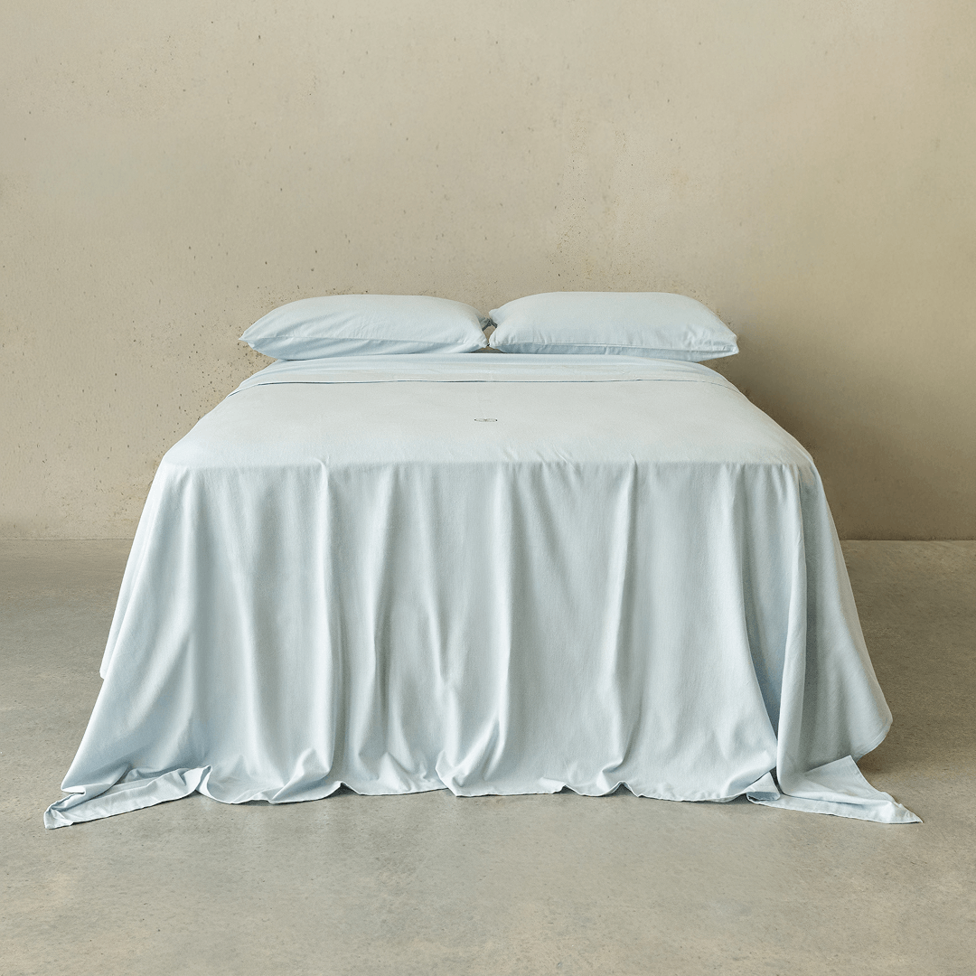 Light blue fitted sheet set styled on a neatly made bed with matching pillowcases, showcasing a clean, minimalist bedroom aesthetic and soft fabric drape.