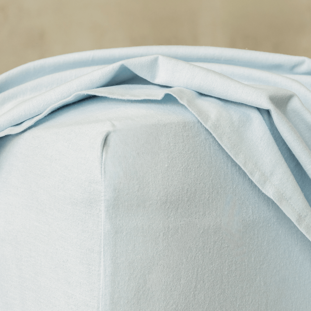 Close-up of a light blue fitted sheet corner, highlighting the elasticized edge designed for a secure and snug mattress fit.