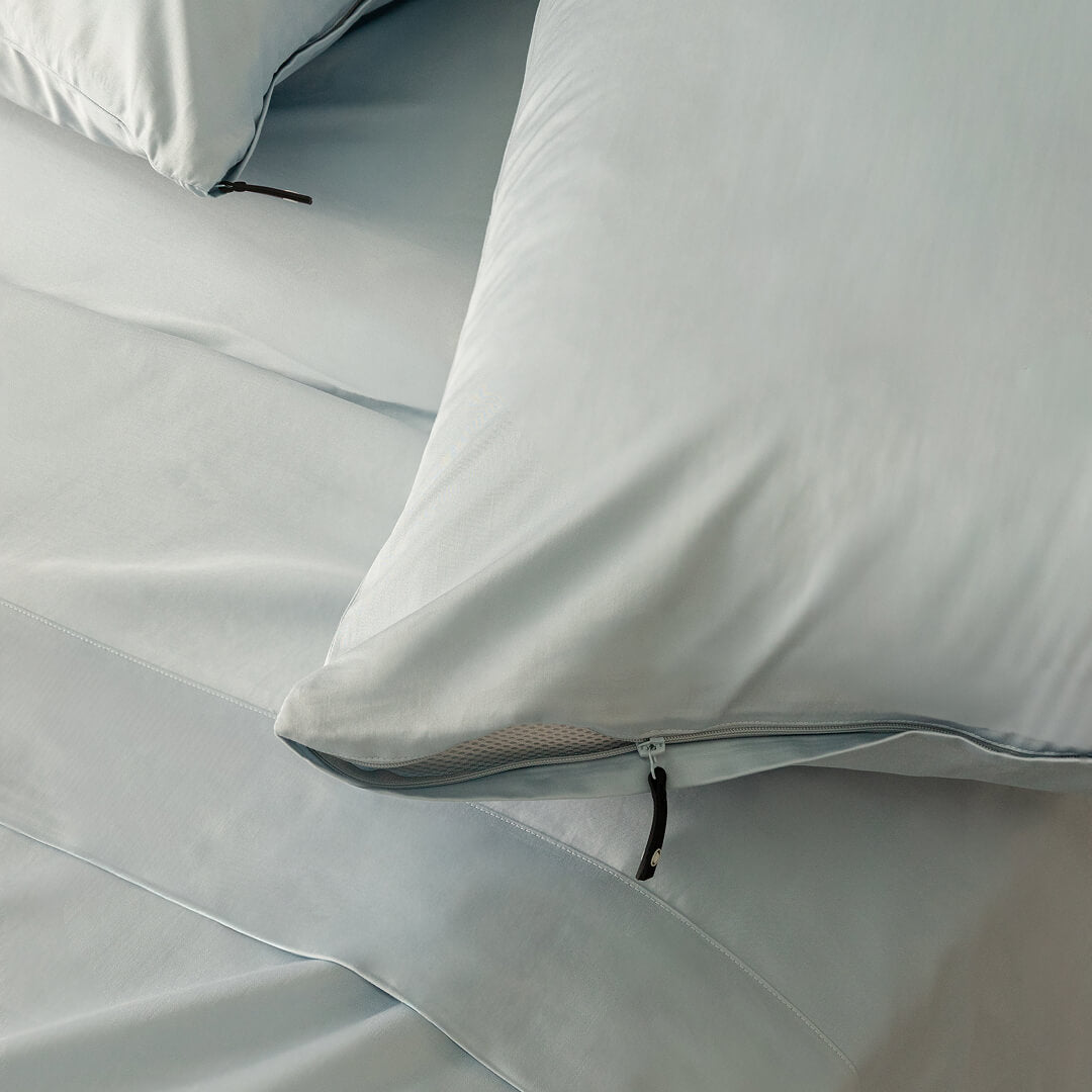 Close-up of light blue pillowcases with a zipper on a bed.