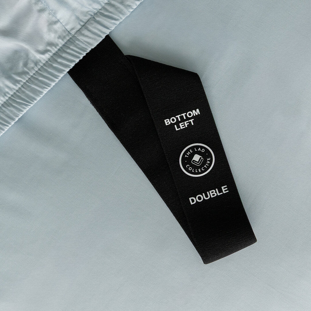 Black labelled loop corner strap with text on a light blue fabric background.