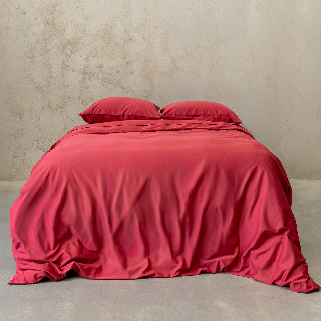 Red quilt cover and pillowcases on a bed against a plain wall.