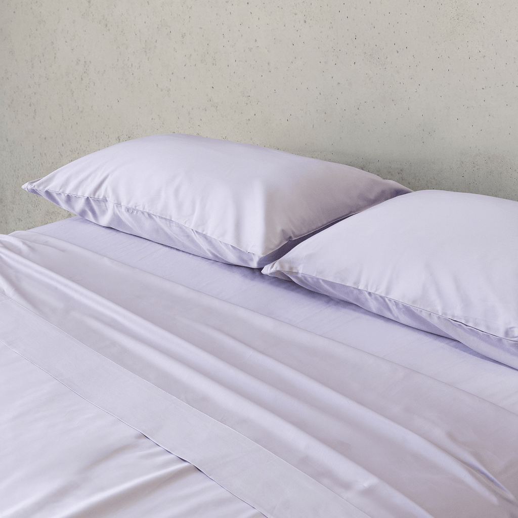 Close-up of two light lavender pillows resting on smooth matching sheets, highlighting the soft fabric and subtle sheen.