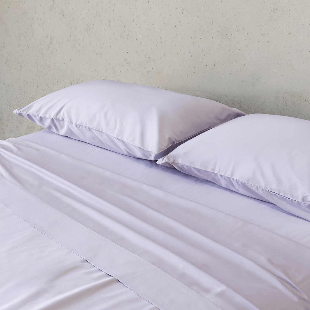 Close-up of two light lavender pillows resting on smooth matching sheets, highlighting the soft fabric and subtle sheen.
