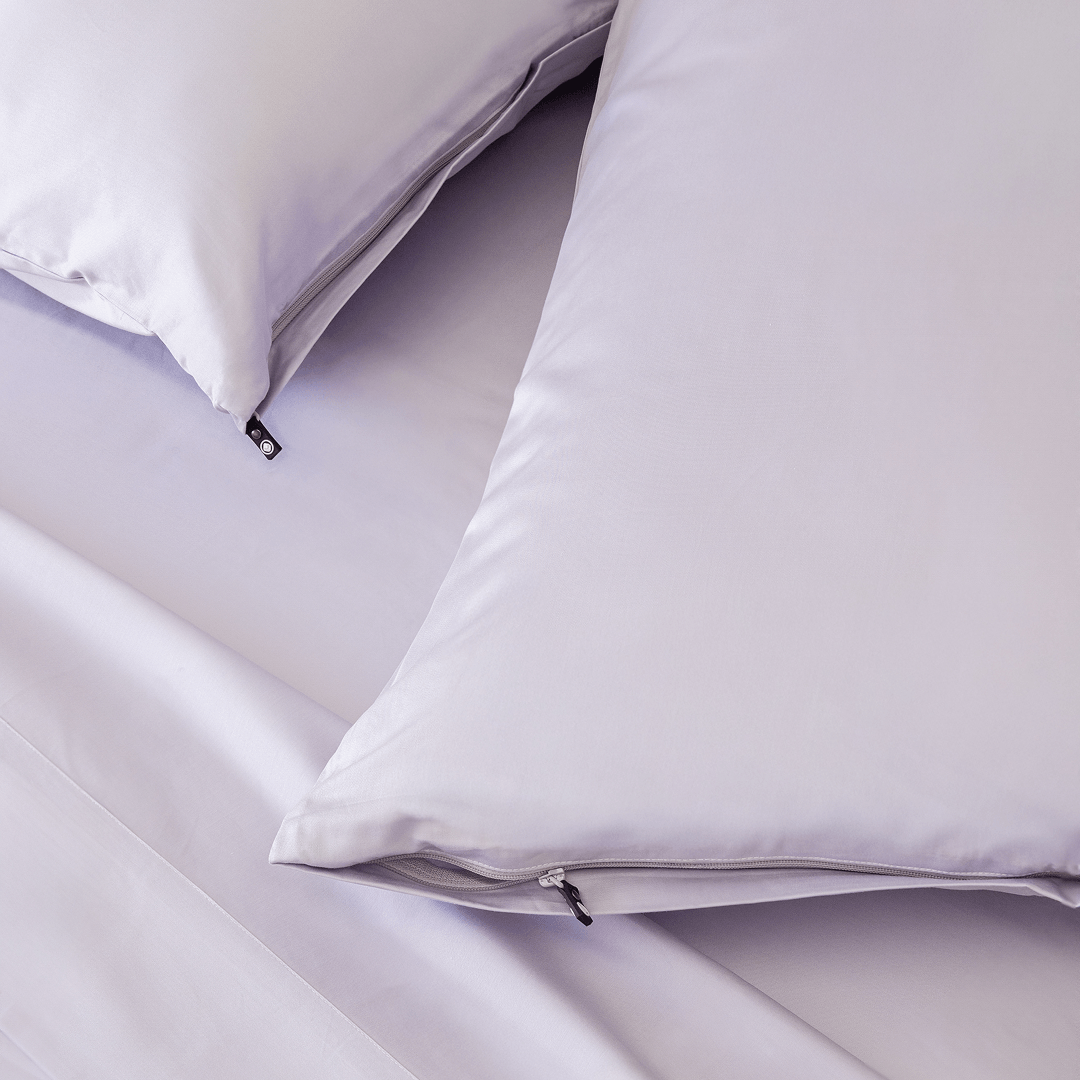Close-up of light lavender pillows with concealed zipper closures and small black branded zipper pulls.