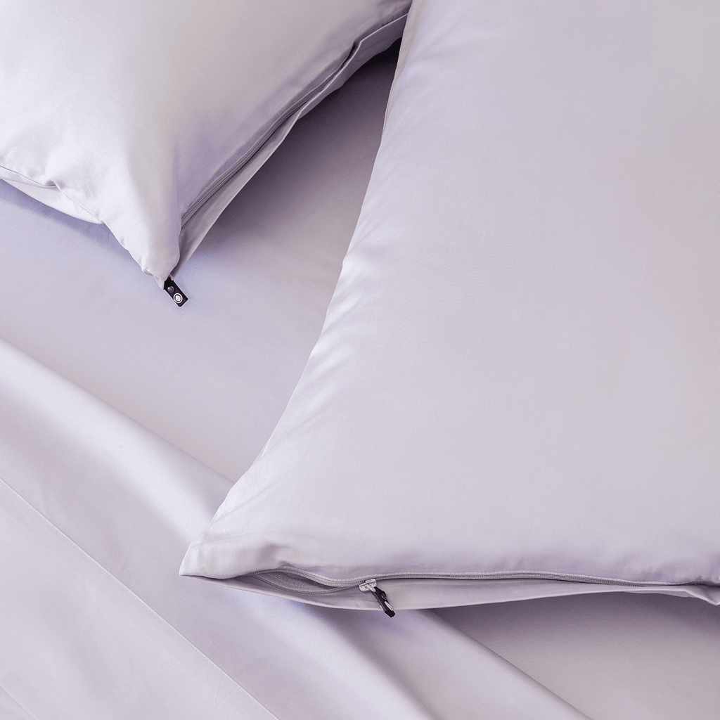 Close-up of light lavender pillows with concealed zipper closures and small black branded zipper pulls.