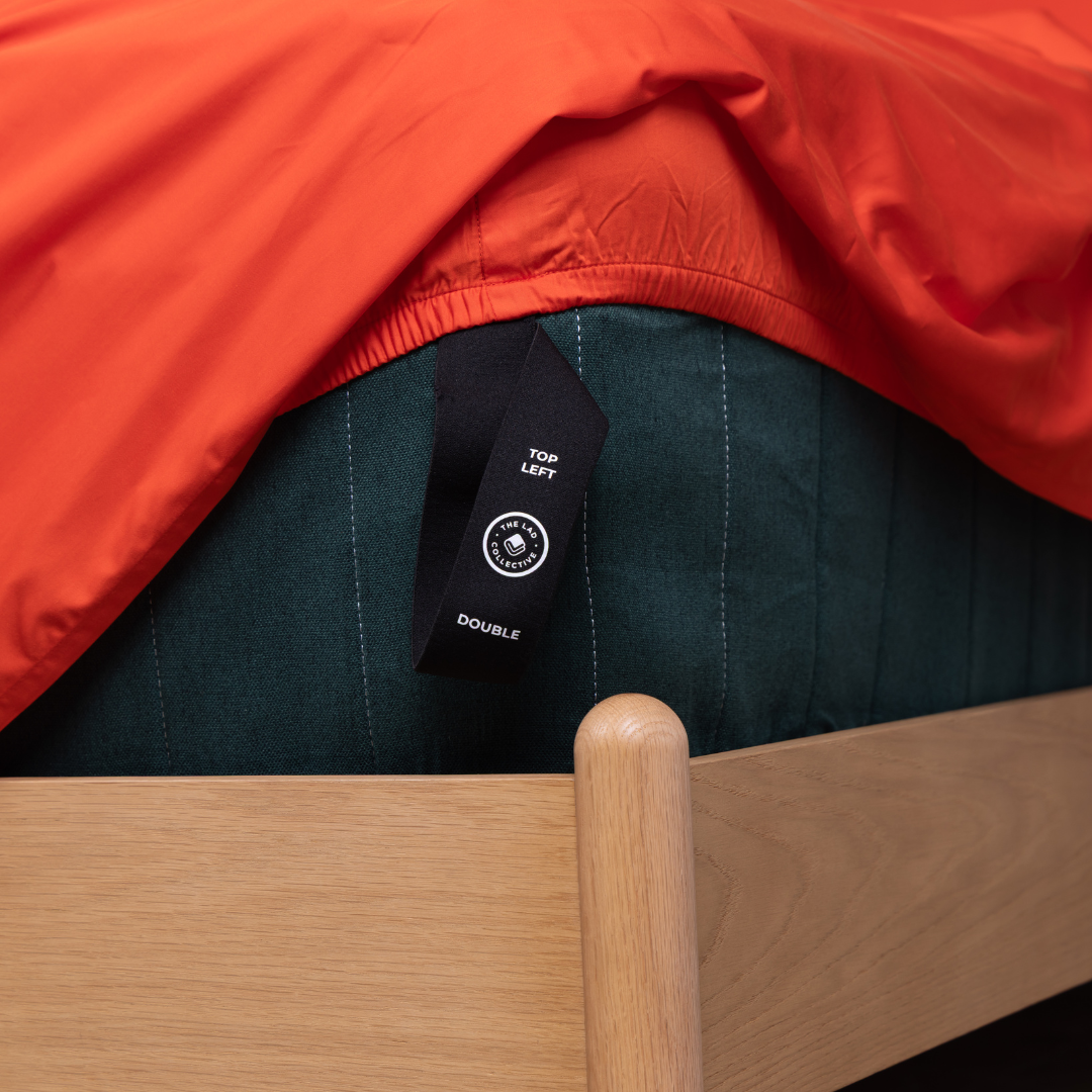 Detailed view of TLC branded label on bamboo cotton fitted sheet corner over black mattress.