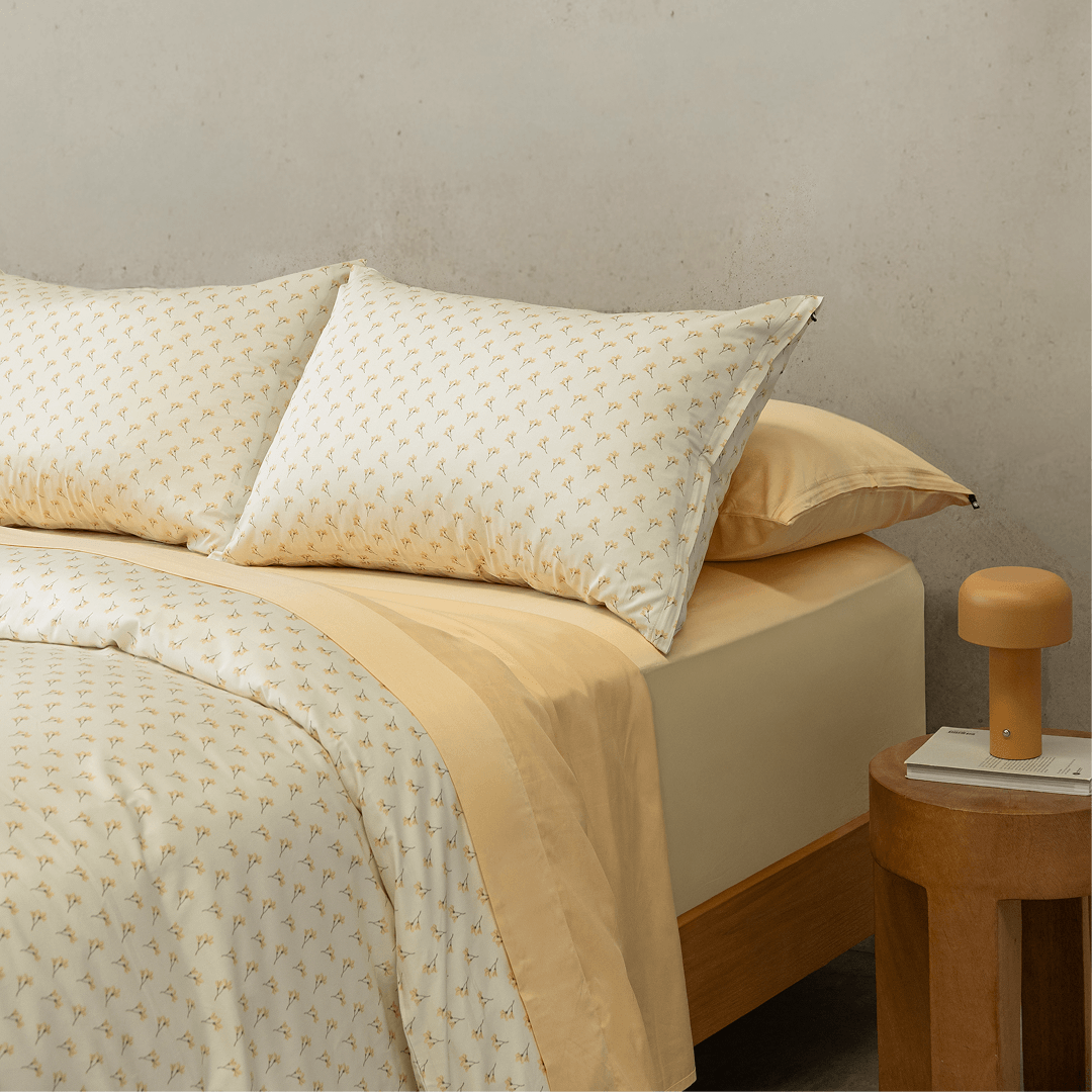 Angle view of a double bed styled with a yellow floral pattern quilt cover over a solid yellow sheet set