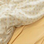 Close-up showing the cream floral print quilt cover folded back to reveal a solid yellow flat sheet underneath