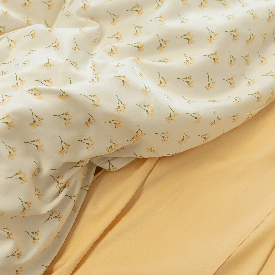 Close-up showing the cream floral print quilt cover folded back to reveal a solid yellow flat sheet underneath